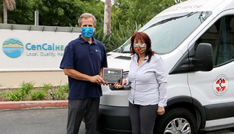 Two humans holding an award plaque in front of the CenCal Health Sign and the Doctors without walls truck.